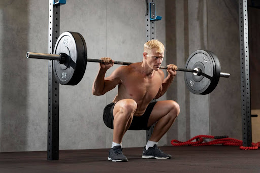a person performing a barbell back squat. This is a compound exercise that targets multiple muscle groups, primarily the quadriceps, hamstrings, and glutes